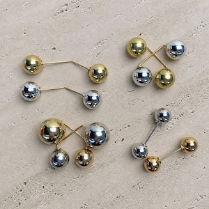 May include: A collection of four double-ended pins featuring polished spherical beads in gold and silver tones. Each pin consists of a thin metal wire connecting two spheres, with some pins featuring mixed metal colours and others featuring matching sets.