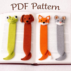 May include: A collection of four crocheted animal bookmarks: a green frog, a brown dog, an orange fox, and a gray mouse. The bookmarks are placed in an open book. The text "PDF Pattern" is at the top.