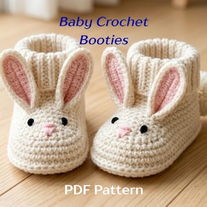 May include: Two cream-coloured crochet baby booties, designed as bunnies, with pink inner ears, black eyes, and a pink nose. The booties have ribbed cuffs and a small pom-pom at the back. The text "Baby Crochet Booties" and "PDF Pattern" are visible.
