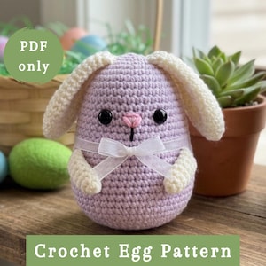 May include: A lavender crochet egg-shaped bunny with cream-colored ears and paws, a pink nose, and black eyes. A white ribbon is tied around the middle. The text "PDF only" and "Crochet Egg Pattern" are visible.
