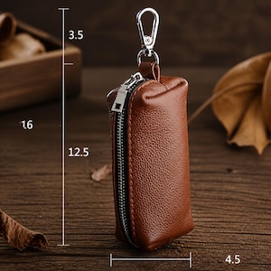 May include: A brown textured leather key pouch with a silver zipper and a silver metal lobster clasp. The pouch features printed dimension markers indicating a height of 12.5 cm, a clasp height of 3.5 cm, and a width of 4.5 cm.