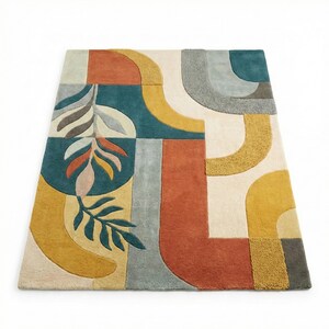 Modern abstract hand-tufted rug with geometric shapes and leaf pattern in teal, mustard, rust, and neutral tones placed in a stylish living room.