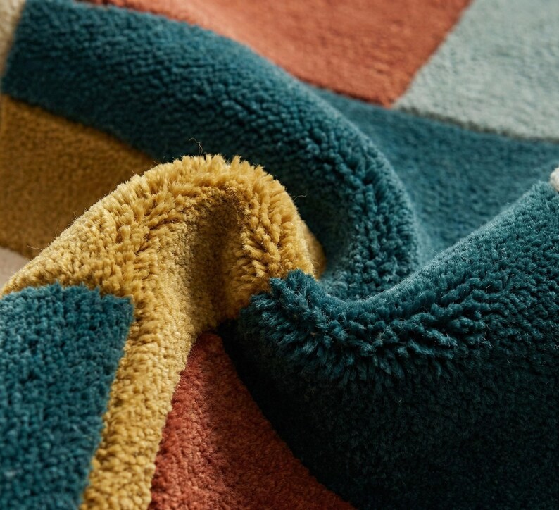 Modern abstract hand-tufted rug with geometric shapes and leaf pattern in teal, mustard, rust, and neutral tones placed in a stylish living room.