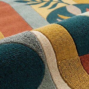Modern abstract hand-tufted rug with geometric shapes and leaf pattern in teal, mustard, rust, and neutral tones placed in a stylish living room.