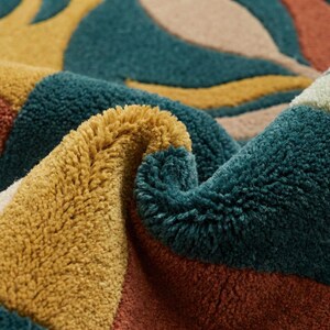 Modern abstract hand-tufted rug with geometric shapes and leaf pattern in teal, mustard, rust, and neutral tones placed in a stylish living room.