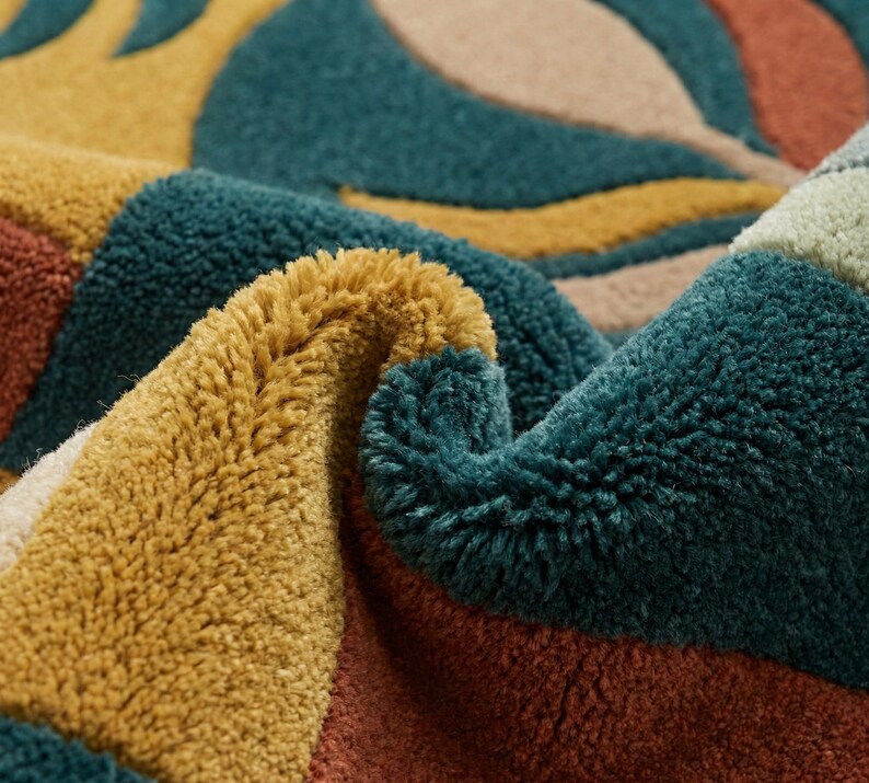 Modern abstract hand-tufted rug with geometric shapes and leaf pattern in teal, mustard, rust, and neutral tones placed in a stylish living room.