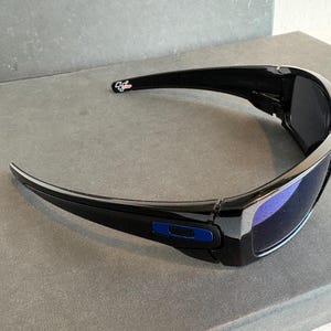 May include: Black sunglasses with a curved design and blue lenses. The sunglasses have a glossy finish and a blue accent on the frame. The sunglasses are designed for outdoor activities.
