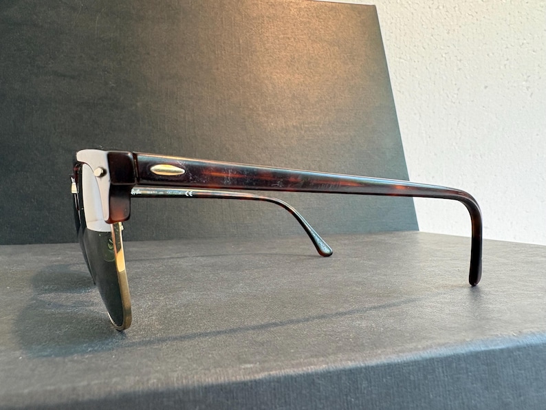 May include: Tortoiseshell-patterned sunglasses with a browline frame design. The frames feature dark brown and amber mottled acetate upper rims and temples, complemented by gold-tone metal lower rims and a small gold-tone accent on the temple hinge.