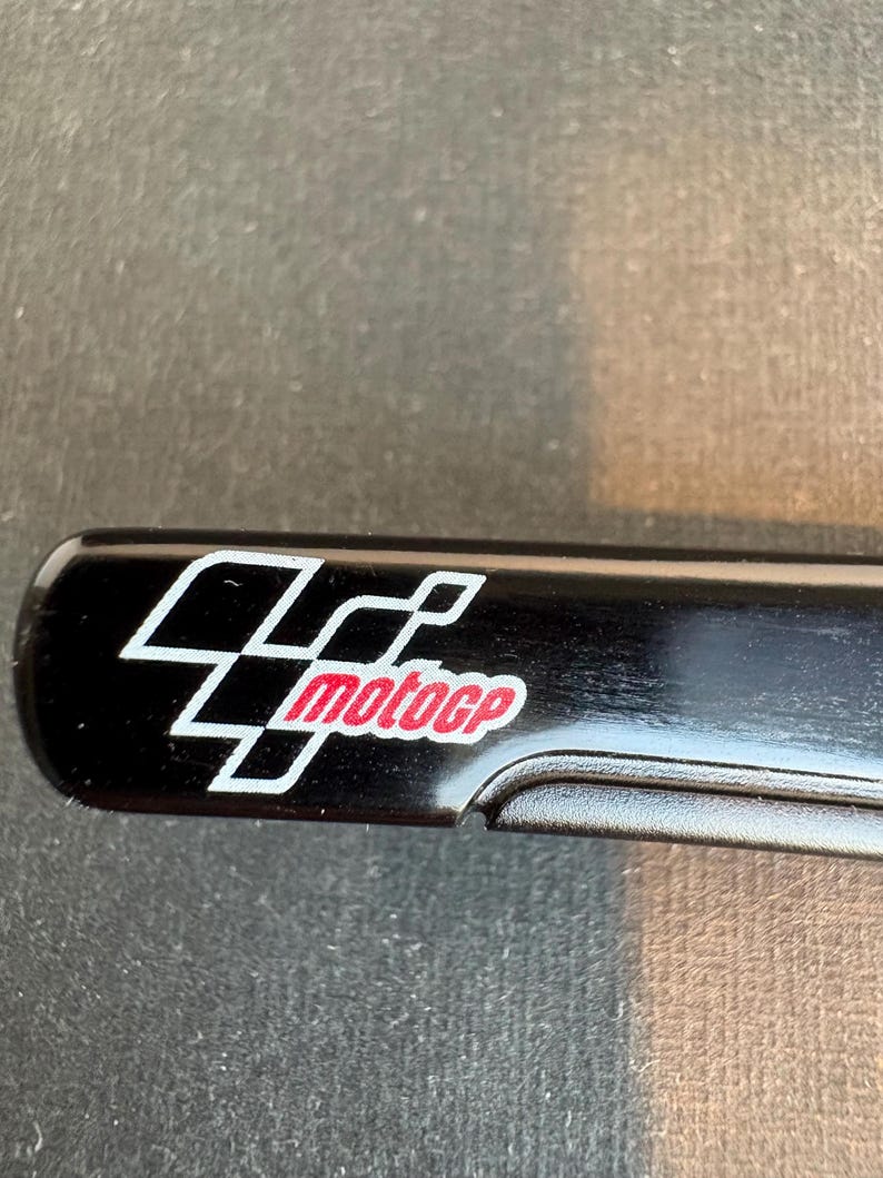 May include: A black rectangular object with the MotoGP logo. The logo features a white and red design with the text "motogp" in red. The object has a curved edge.