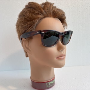 May include: Tortoiseshell sunglasses with dark lenses. The frames are rectangular and are displayed on a mannequin head. A classic style of eyewear.