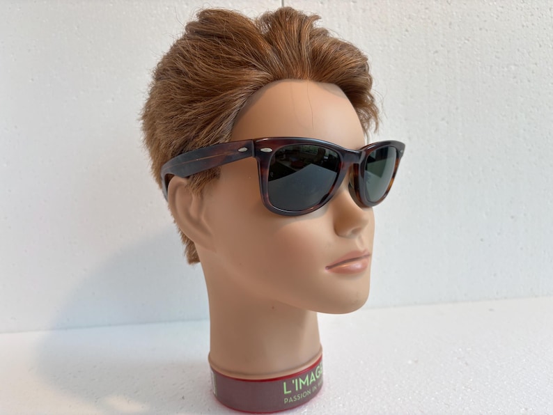 May include: Tortoiseshell sunglasses with dark lenses. The frames are rectangular and are displayed on a mannequin head. A classic style of eyewear.