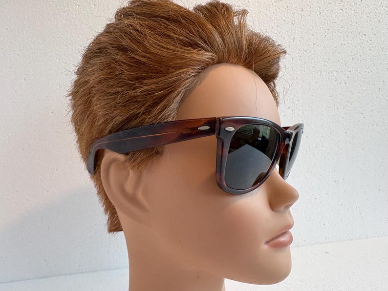 May include: Dark brown tortoiseshell sunglasses with square frames and dark lenses. The image shows the sunglasses on a mannequin head with brown hair.