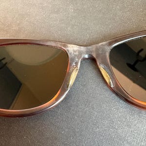 May include: Close-up of brown sunglasses with dark lenses. The frames have a mottled, translucent appearance. The lenses are dark, and the bridge of the glasses is visible.