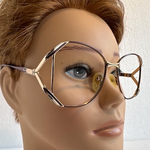 Könnte beinhalten: Vintage Brille mit geometrischem Design. Die Fassungen sind eine Kombination aus Gold, Braun und Silber. Die Gläser sind hellgelb. Die Brille befindet sich auf einem Schaufensterkopf.