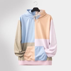 May include: Color block hoodie in pastel shades of blue, peach, pink, and tan. The hoodie features a drawstring hood, a kangaroo pocket, and ribbed cuffs and hem. The garment is hanging on a black hanger.