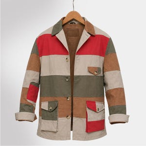 Puede incluir: Chaqueta patchwork multicolor con cuello, botones y dos bolsillos delanteros. La chaqueta presenta paneles rojos, marrones, verdes y beige. Las mangas están dobladas y la chaqueta está colgada de una percha de madera.