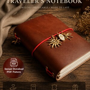 May include: A brown leather traveller's notebook featuring a red elastic band closure with three metal charms: a sun, a floral oval, and a bow. The cover displays text reading HANDMADE TRAVELLER'S NOTEBOOK, TIMELESS, REFILLABLE, MADE TO LAST.