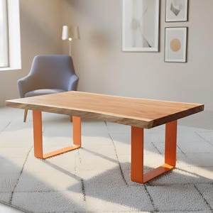 Può includere: Tavolino rettangolare in legno con finitura a venature naturali. Il tavolo ha gambe in metallo arancione brillante. Il tavolo è appoggiato su un tappeto bianco con un motivo geometrico. La stanza ha un design moderno.
