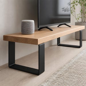 May include: A light oak TV stand with a rectangular wooden top and black metal legs. The stand supports a flat-screen TV and a grey speaker. The design is modern and minimalist, suitable for a living room. The stand is approximately 150cm long.