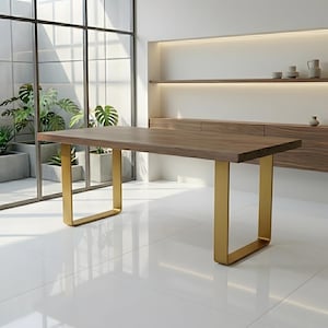 Puede incluir: Una mesa de comedor rectangular con un tablero de madera marrón oscuro grueso con borde natural y dos patas de metal dorado en forma de U. La mesa está situada en una habitación luminosa con suelo de baldosas blancas y grandes ventanales.