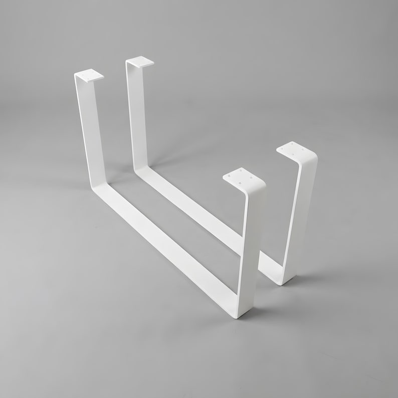 May include: Two U-shaped metal table legs finished in a matte white powder coating. Each leg features a flat mounting plate at the top with pre-drilled holes for attachment, connected to two vertical supports joined by a long horizontal base bar.