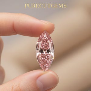 Può includere: Un diamante rosa a taglio marquise tenuto tra due dita. La gemma ha molte sfaccettature, che riflettono la luce. Il testo "PURECUTGEMS" è in lettere dorate nella parte superiore dell'immagine. Il diamante è di colore rosa chiaro.