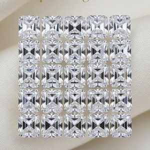 May include: Twenty-five clear, radiant-cut gemstones, arranged in a grid. Each square gem has beveled edges, reflecting light. The text "purecutgems" is visible. The background is a soft, off-white fabric, creating a subtle contrast.