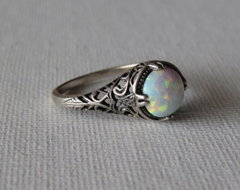 Könnte beinhalten: Ein silberner Ring mit einem Opal-Edelstein, der in einem filigranen Design gefasst ist.