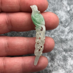 May include: A carved jade bird pendant with a green and white color scheme. The bird is perched on a branch with intricate details.