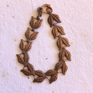 May include: A copper bracelet with a leaf design. The bracelet is made of individual copper leaves that are linked together. The clasp is marked "COPPER".