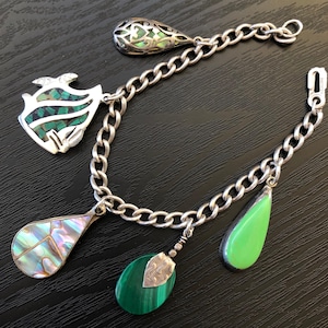 May include: A silver charm bracelet with five charms. The charms are a green and silver fish, a green and silver teardrop, a green and silver teardrop, a green and silver teardrop, and a green and silver oval.