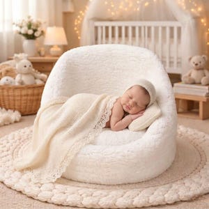 May include: A newborn baby sleeps peacefully on a soft, white, plush chair, wrapped in a cream-colored blanket with a delicate lace trim. The baby wears a matching cap and rests on a small pillow. The scene is set in a nursery with a neutral color palette.