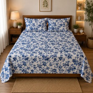 Peut inclure: Un ensemble de lit composé d'un drap blanc à motif floral bleu dense, recouvrant le matelas, accompagné de deux oreillers rectangulaires assortis disposés contre la tête de lit d'un cadre de lit en bois.