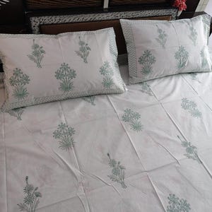 Può includere: Un set di lenzuola bianche composto da due federe abbinate e un lenzuolo, decorato con un motivo ripetuto di bouquet di fiori verde chiaro. I bordi delle federe sono rifiniti con una sottile bordura a chevron di colore verde chiaro.