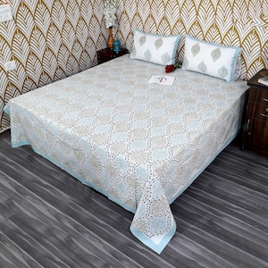 Peut inclure: Un lit avec une housse de couette à motifs gris et bleu clair et des taies d'oreiller assorties. La housse de couette présente un motif géométrique répétitif avec une bordure bleu clair. Deux taies d'oreiller blanches avec un motif de feuilles sont sur le lit.