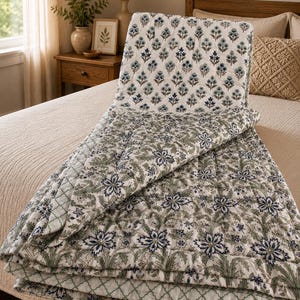 May include: A reversible quilted bedspread featuring two distinct patterns. One side displays a small-scale blue and green floral print on a white background, while the other side showcases a larger, intricate blue and green floral motif.