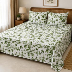 May include: A white bed sheet set featuring a repeating botanical pattern of green leaves and small white flowers. The set includes a flat sheet covering the mattress and two matching rectangular pillowcases placed against a wooden headboard.