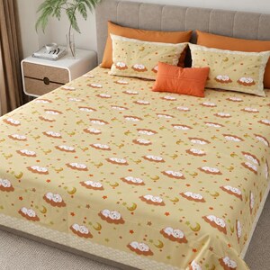May include: A bed sheet set featuring a light yellow background with a repeating pattern of white sleeping sheep on brown clouds, yellow crescent moons, and orange stars. The set includes two rectangular pillows and one small orange accent pillow.