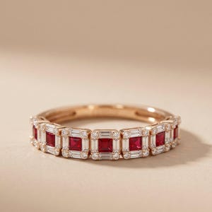 May include: A rose gold ring featuring a series of square-cut red gemstones alternating with rectangular white gemstones. Small, round white gemstones are set between the rectangular stones. The ring is displayed on a neutral background.