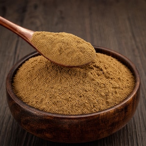 May include: A dark brown wooden bowl filled with a fine, light brown powder, accompanied by a matching wooden spoon also containing a portion of the same finely ground, textured, light brown substance, showcasing a consistent earthy tone.
