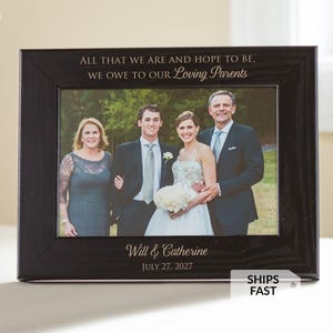 May include: Black wooden picture frame with a family photo. The frame has the inscription "ALL THAT WE ARE AND HOPE TO BE, WE OWE TO OUR Loving Parents." The names "Will & Catherine" and the date "JULY 27, 2027" are also inscribed.