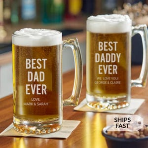 May include: Two clear glass beer mugs with thick handles, each filled with golden beer and white foam. The left mug features the white text BEST DAD EVER LOVE, MARK & SARAH. The right mug features the white text BEST DADDY EVER WE LOVE YOU! GEORGE & CLAIRE.