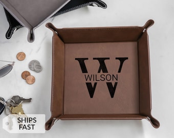 May include: A brown leather valet tray with the name "WILSON" and a large "W" printed in black. The tray has a square shape with rounded corners. Other trays and coins are also visible.