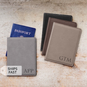 May include: A collection of personalized passport holders in various colors, including gray, brown, and black. One gray holder contains a blue passport. The holders are embossed with initials. The image also includes the text "SHIPS FAST".