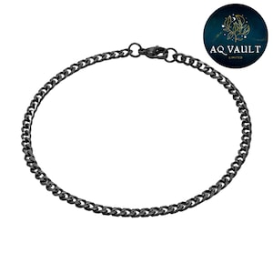 May include: A black curb chain bracelet. The bracelet is made of small, interlocking links and features a lobster clasp closure. The bracelet is shown on a white background. A circular logo with the text "AQ VAULT LIMITED" is in the upper right corner.
