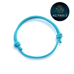 May include: A bright turquoise rope bracelet with adjustable knots. The bracelet is a vibrant blue and designed for the wrist. The background is white, with a circular logo in the top right corner. The bracelet's circumference is approximately 15 cm.
