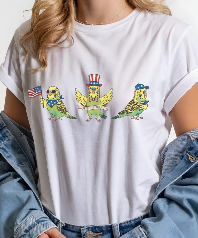 May include: White t-shirt featuring three cartoon parakeets celebrating the 4th of July. One parakeet holds an American flag, another wears a top hat, and the third wears a baseball cap. The text "4th of July" is on a banner.