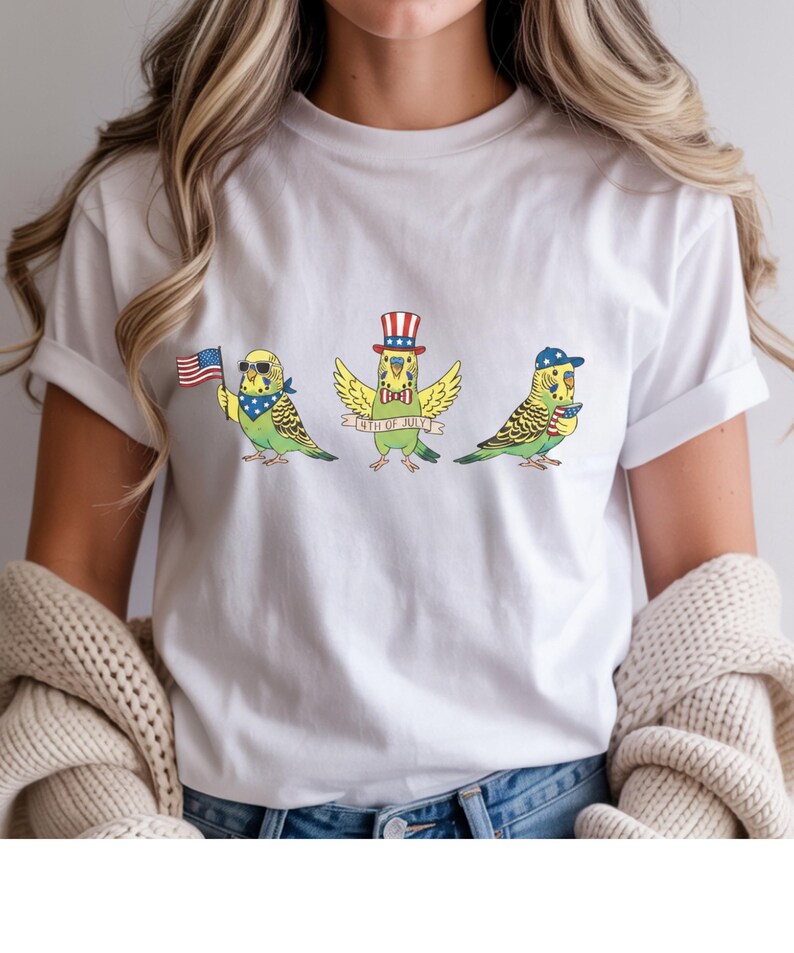 May include: White t-shirt featuring three cartoon parakeets celebrating the 4th of July. Each parakeet is adorned with patriotic accessories: sunglasses and a bandana, a top hat, and a baseball cap. The middle parakeet has a banner that reads "4th of July".