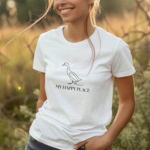 Puede incluir: Camiseta blanca con un dibujo lineal minimalista de un pato y el texto "MY HAPPY PLACE" en negro. La camiseta es de cuello redondo.