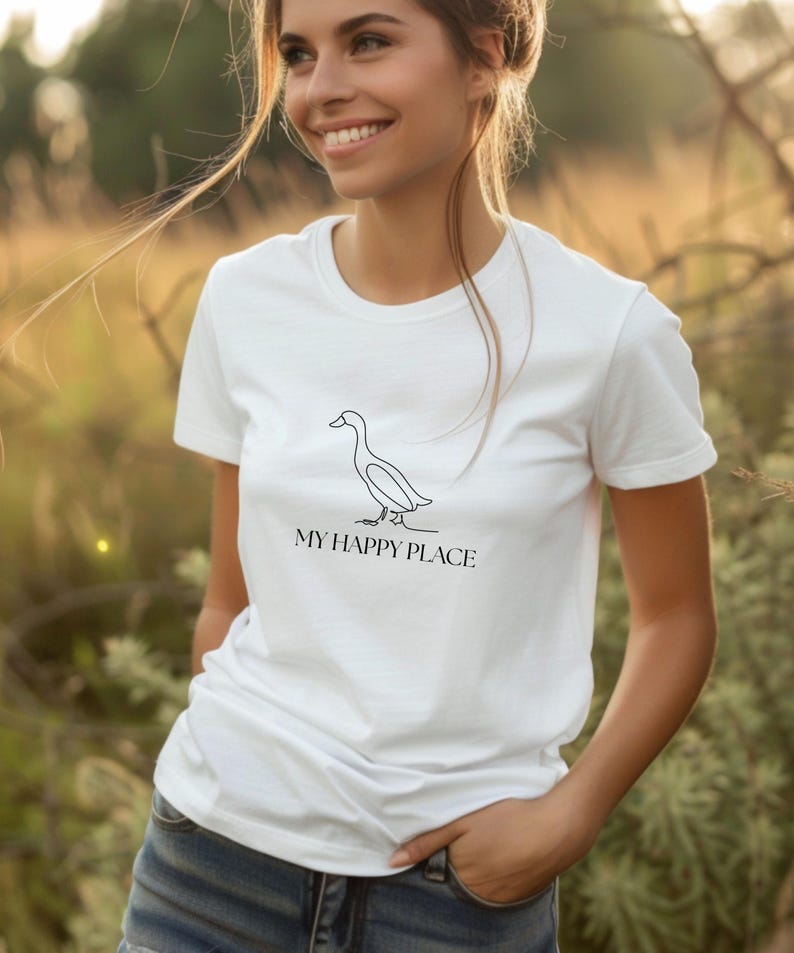 Puede incluir: Camiseta blanca con un dibujo lineal minimalista de un pato y el texto "MY HAPPY PLACE" en negro. La camiseta es de cuello redondo.